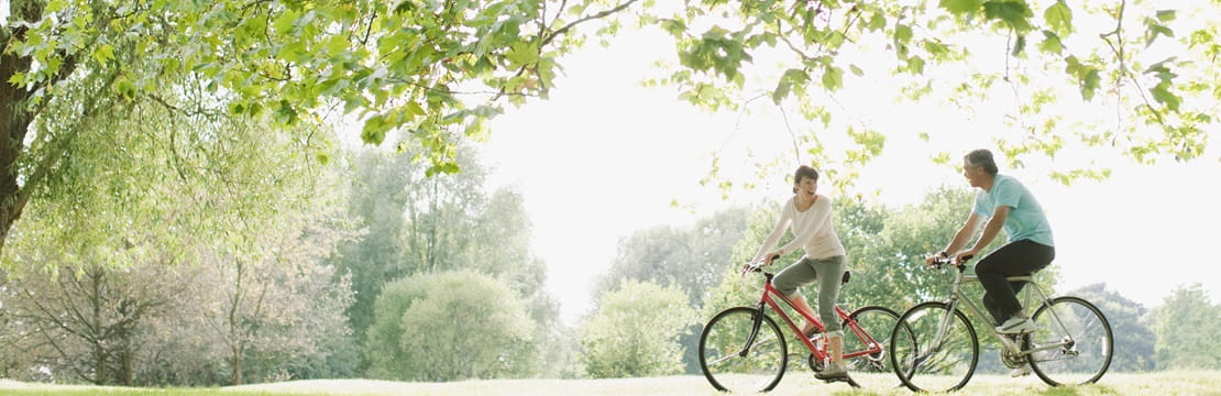 Mature couple riding bicycles in a park.